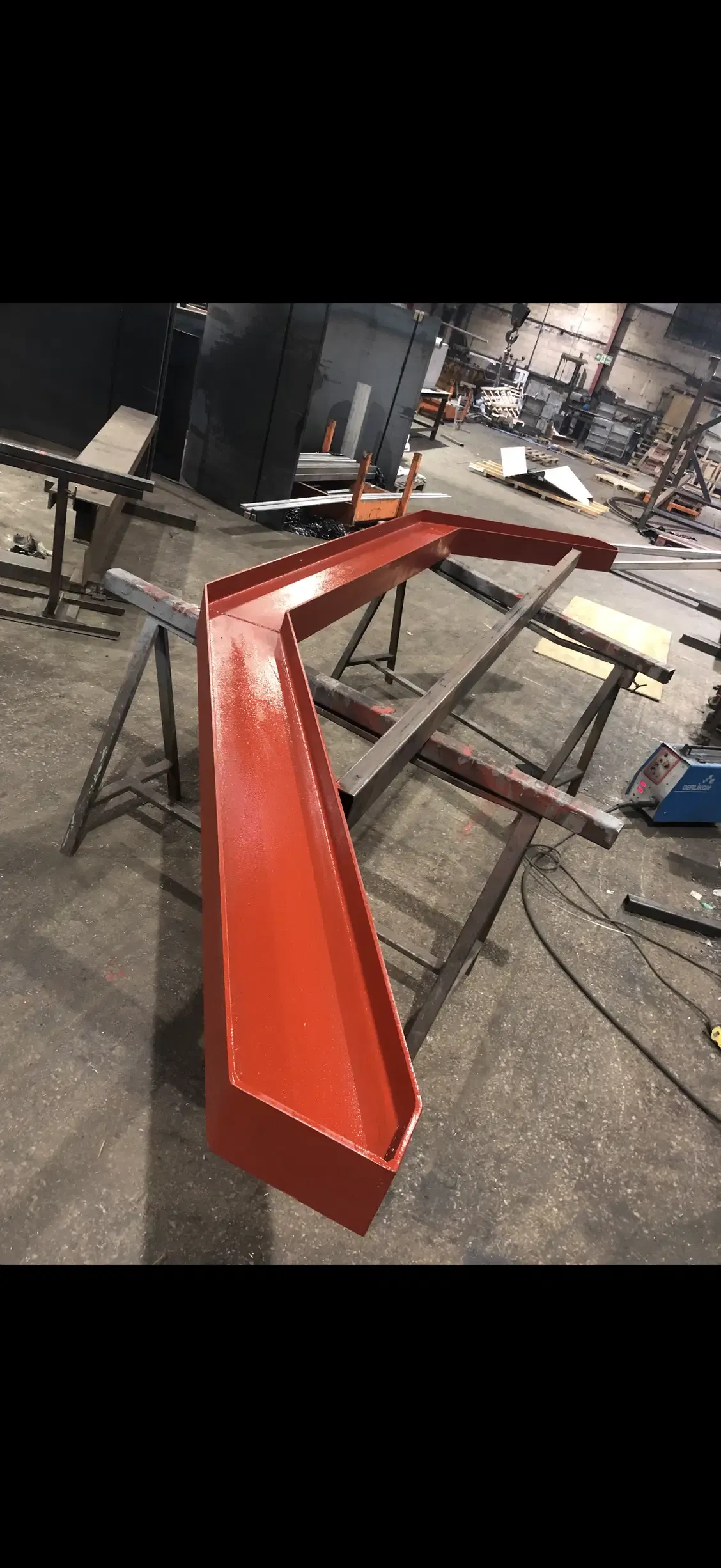 Large red-oxide coated folded steel trough section supported on workshop trestles